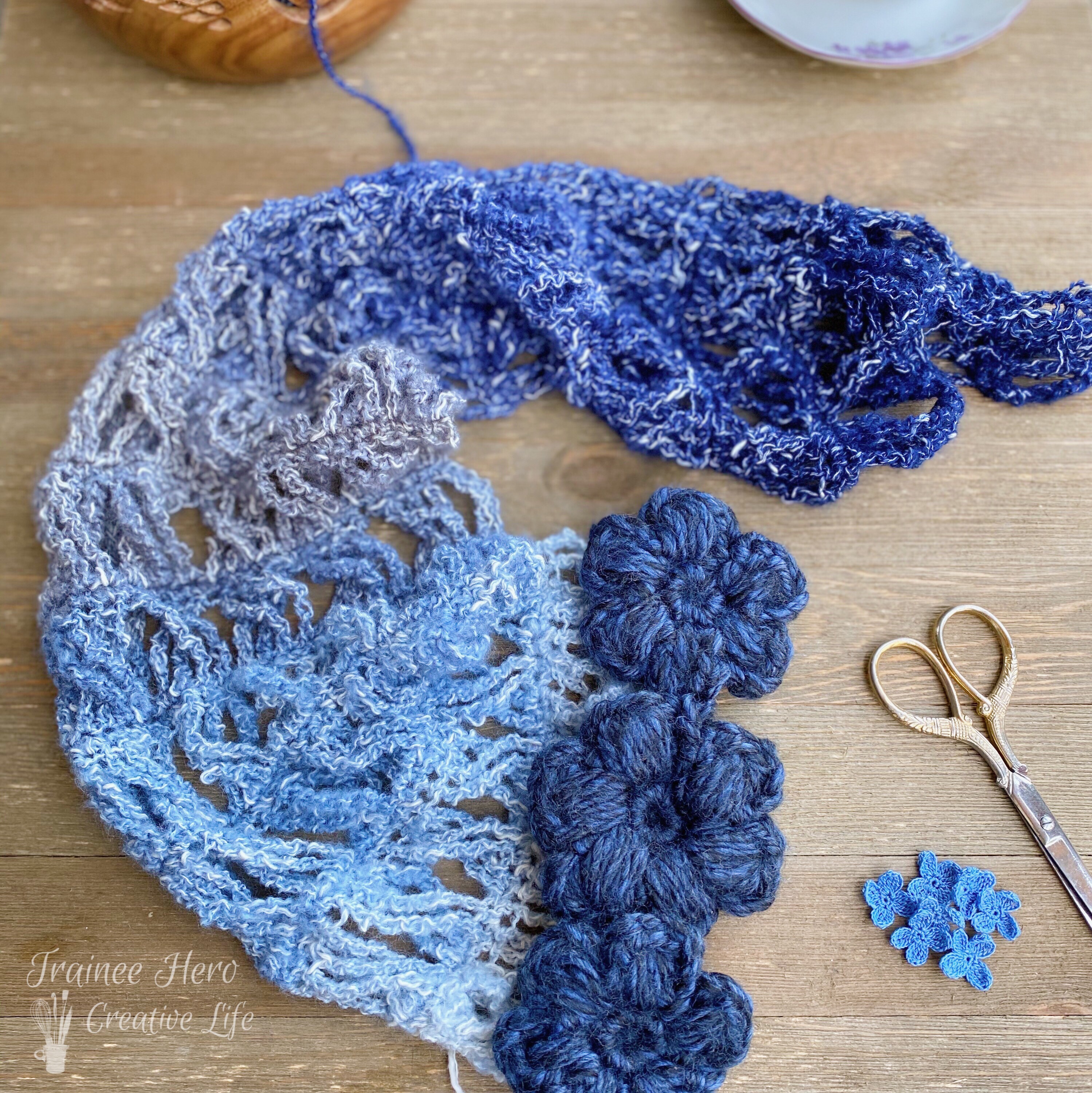 The convertible crochet scarf laid out in a curve with crochet puff stitch flowers