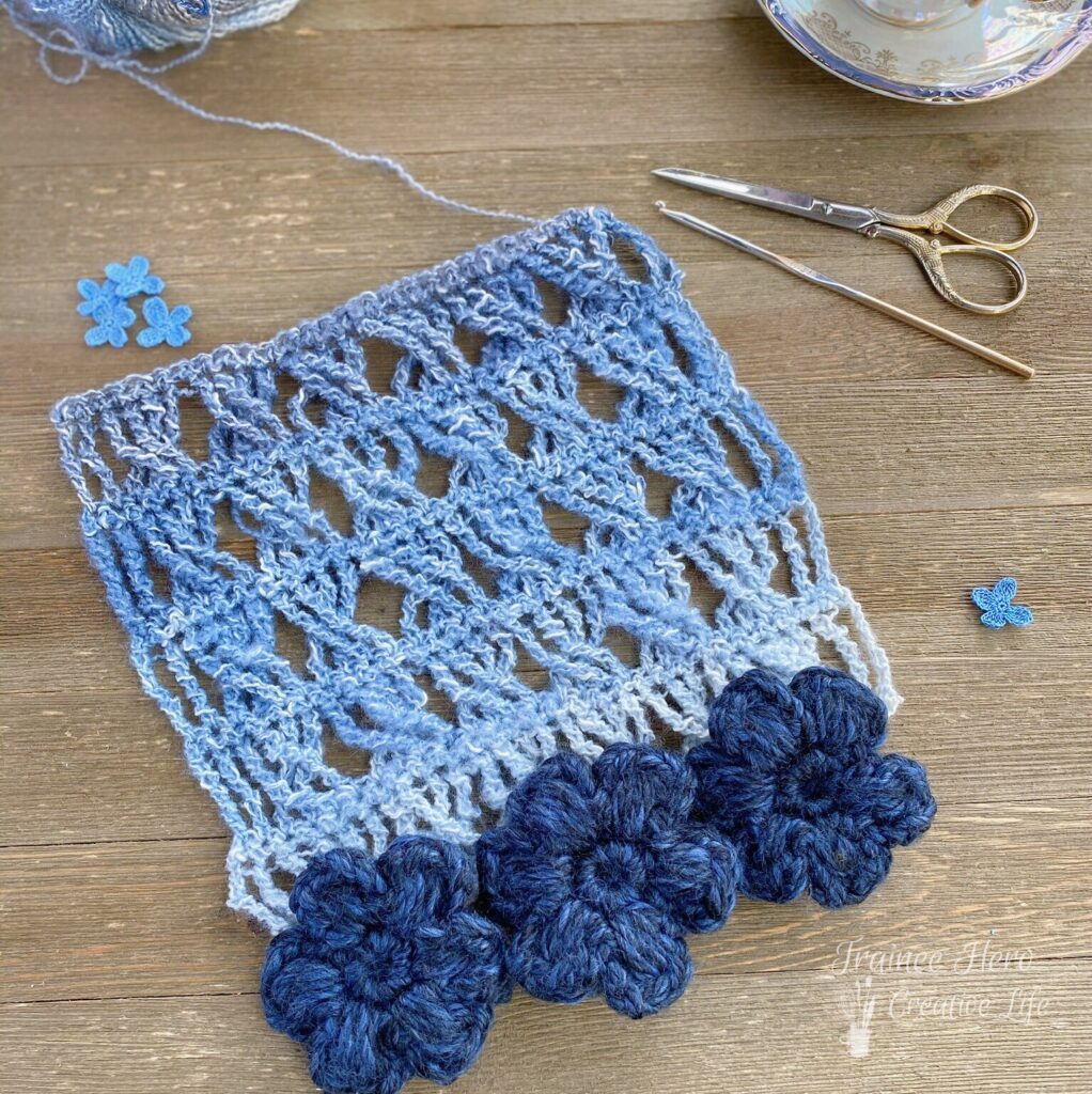 First few rows of the convertible crochet scarf. Shows the stitch pattern up close and has puff stitch flowers laid out on the edge.